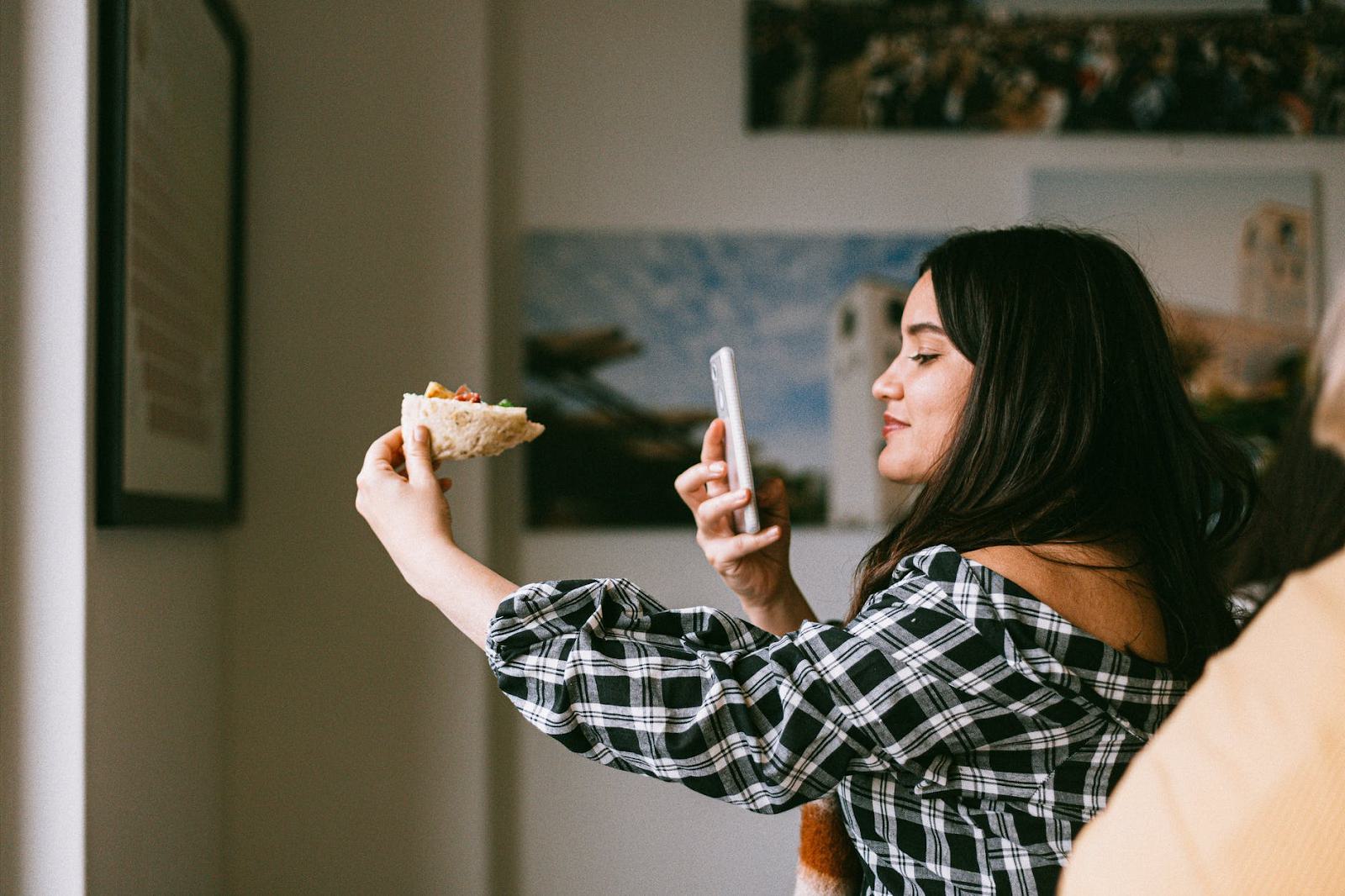 Photo of a woman taking a picture of a slice of pizza with her phone.